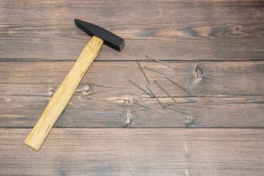 Tahta saplı bir inşaat çekici kahverengi zeminde solda yatıyor. Çekiç ve çiviler tahtada, kahverengi tahtalarda.