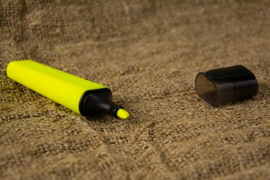 Sarı fosforlu kalem gri bir kumaşın üzerinde. Eski sarı çuval bezi üzerine kırtasiye malzemesi.