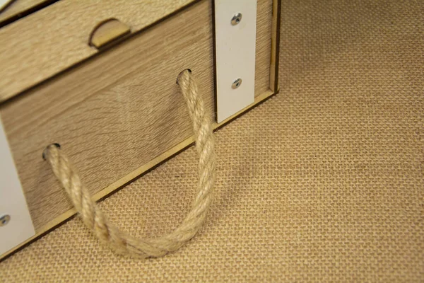 A gray vintage box with a rope handle on a beige burlap background. Antique, wooden product on the table close-up.