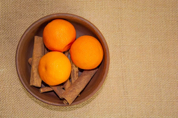 Çuval beziyle kaplı bir masada tarçın ve mandalina içeren kil bir vazo. Üst Manzara. Masadaki kahverengi çömlek.