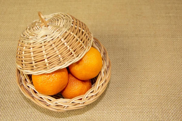 Çuval beziyle kaplı bir masanın kapağıyla kaplı mandalinalı hasır bir sepet. Bej arkaplanda hasır tabaklar.