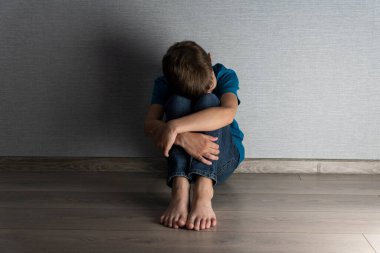 Karanlık odada yalnız bir çocuk yerde oturur ve yüzünü dizlerine saklar. İstismar, ceza, ev içi şiddet kavramı