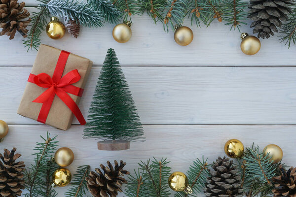 Вид сверху на игрушечную елку и обернутую подарочную коробку, украшенную ветвями сосны и шишками на белом деревянном фоне, копировальное пространство. Рождественский консент                              