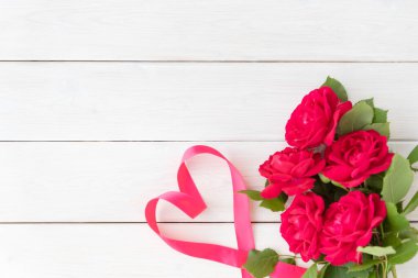 Beş kırmızı gül ve beyaz ahşap arka planda kalp şeklinde pembe kurdele. Selamlar konsepti