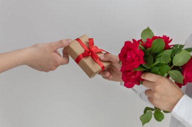 Erkek elinin kıza hediye kutusu vermesi ve bir buket kırmızı gül, açık arkaplan, fotokopi alanı. Sevgililer Günü ve Tebrik Konsepti