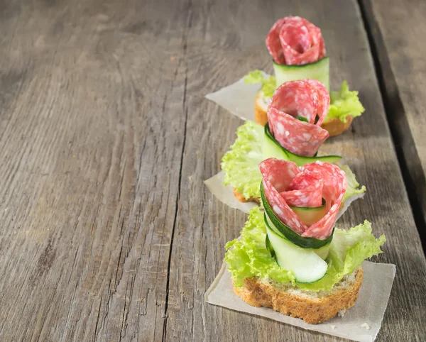 Canapé com salame, pepino e salada em mesa de madeira — Fotografia de Stock