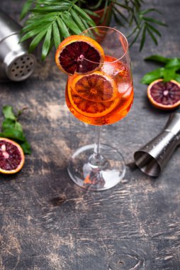 Kanlı portakallı büyük şarap kadehinde Aperol sprey kokteyli, kırmızı acı, kuru beyaz şarap, soda, tat ve buz koyu arka planda, bar aletleri..