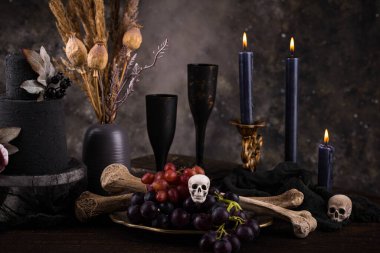 Halloween still life with skull, bones, candles and black cake. Dark table setting
