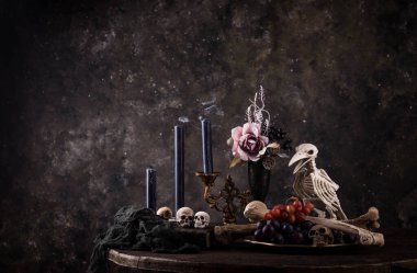 Halloween still life with skull, bones, candles and black cake. Dark table setting
