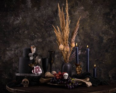 Halloween still life with skull, bones, candles and black cake. Dark table setting