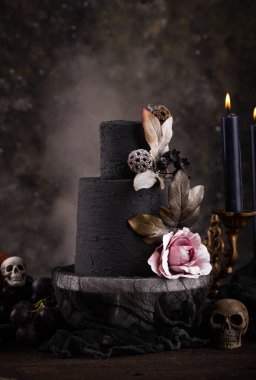 Halloween still life with skull, bones, candles and black cake. Dark table setting