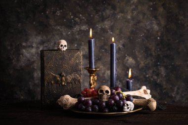 Halloween still life with skull, bones, candles and black cake. Dark table setting