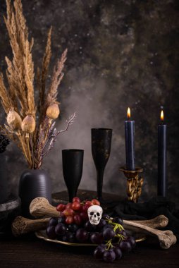 Halloween still life with skull, bones, candles and black cake. Dark table setting