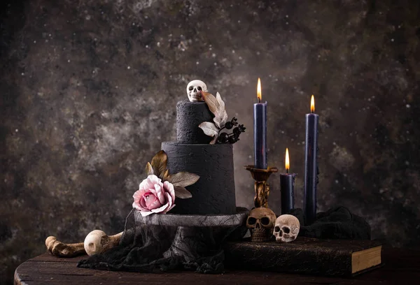 Halloween still life with skull, bones, candles and black cake. Dark table setting