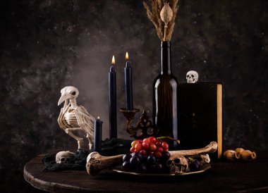 Halloween still life with skull, bones, candles and black cake. Dark table setting