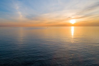 Sakin denizin üzerinde gün batımı, uzakta küçük bir tekne ve metin alanı.