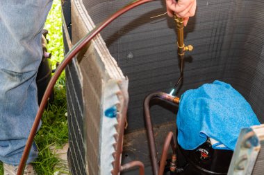 Klima teknisyeni ekipmanları onarmak için bir meşale kullanıyor.