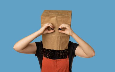 Woman wearing paper bag over her head holding her hands near eyes like binoculars