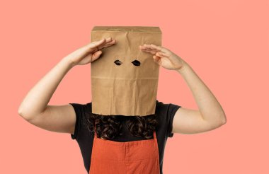 Young woman wearing paper bag over her head with hands above eyes, searching.