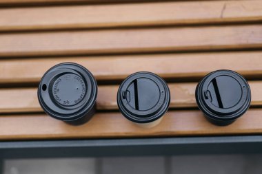 Parktaki bankta duran kapaklı kahve bardağı. Yaz günü, güneş ışınları ve parıltıları. Sıcak renk tonu.