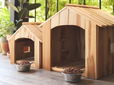İki boş ahşap köpeğin evinin yan görüntüsü. Balkonda köpek maması kaseleri var. Çiçek saksısıyla süslenmiş..