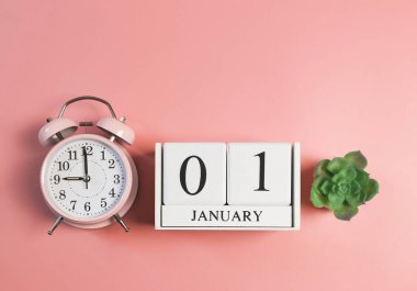 Ahşap takvimin üst görüntüsü 01 Ocak, pembe alarmlı saat 9 yönünde ve pembe arka planda sulu bitki saksısı. Yeni yılın ilk sabahı.