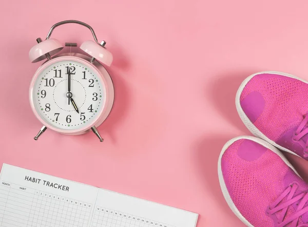 Üst görünüm ya da düz alışkanlık takip kitabı, pembe spor ayakkabılar ve pembe alarm saati saat 5 'te fotokopi alanı olan pembe arka planda. Spor ve sabah rutini ve kişisel gelişim.