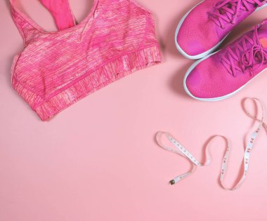 Üst ya da düz pembe spor ayakkabılar, pembe spor sutyen ve pembe arka planda fotokopi alanı ile ölçü bandı. Spor ve kilo verme konsepti.