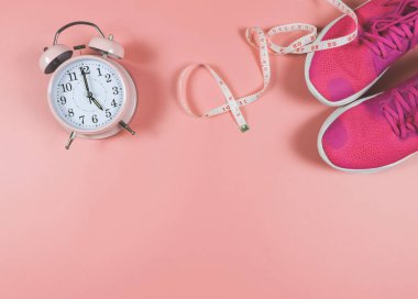 Üst ya da düz pembe spor ayakkabılar ya da spor ayakkabılar, pembe çalar saat ve pembe arka planda fotokopi alanı olan mezura. Spor ve kilo verme konsepti.