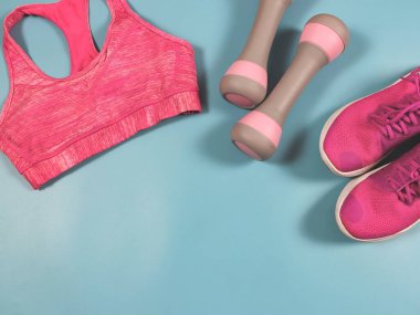 Üst ya da düz pembe spor ayakkabı yatağı, pembe spor sutyen ve pembe arka planda pembe renkli gri halterler fotokopi alanı. Spor ve aktif yaşam tarzı kavramı.