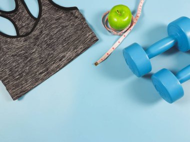 Üst ya da düz gri spor sutyen, mavi halterler, yeşil elma ve mavi arka planda fotokopi alanı olan mezura. etkin yaşam tarzı ve kilo verme kavramı.