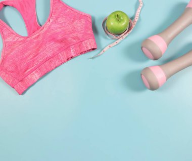 Üst ya da düz pembe spor sutyen yatağı, gri pembe halterler, yeşil elma ve mavi arka planda fotokopi alanı olan mezura. etkin yaşam tarzı ve kilo verme kavramı.