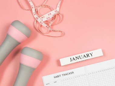 Üst ya da düz alışkanlık takip kitabı, ahşap takvim Ocak, gri pembe dambıllar ve pembe arka planda fotokopi alanı ile ölçüm bandı. Kişisel gelişim ve aktif yaşam tarzı kavramı.