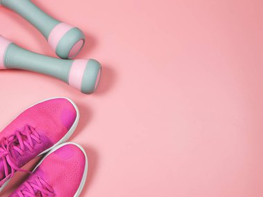 Üst ya da düz pembe spor ayakkabıları ya da spor ayakkabıları ve pembe arka planda gri pembe halterler fotokopi alanı. Spor ve aktif yaşam tarzı kavramı.