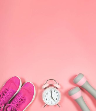 Saat 5 yönünde pembe alarm saati, pembe spor ayakkabılar ya da pembe arka planda pembe halterler ve fotokopi alanı. Aktif yaşam tarzı ve sabah rutini kavramı.