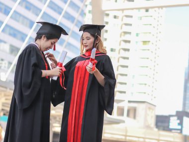 Portrait of Two cheerful graduated women in graduation gowns, helping each other dress up, smiling happily. Education, successful and friendship concept.