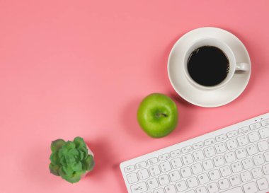 Top view of  Green apple with black coffee cup, computer keyboard, succulent plant pot on pink background with copy space.  Healthy snack and lunch with working in office. Healthy Lifestyle Concept