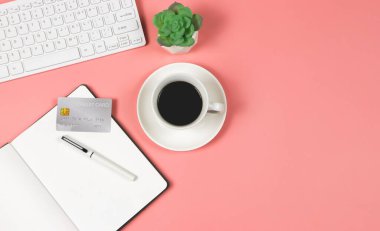 Top view or flat lay of credit card on open note book, pen, black coffee cup, computer keyboard and succulent plant pot on pink bakcground. Financial planning concept.