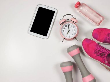 Üst ya da düz pembe antika çalar saat, spor ayakkabılar, dambıllar, su şişesi ve beyaz arkaplanda boş ekran dijital tablet. Sağlıklı yaşam tarzı kavramı.