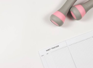 Üst ya da düz alışkanlık takip kitabı, beyaz arka planda gri pembe dambıllar ve fotokopi alanı. etkin yaşam tarzı ve kişisel gelişim kavramı.