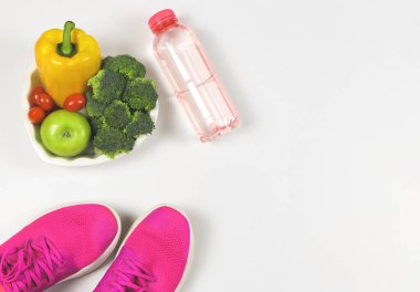 Sebze kapsisi, brokoli, domates ve elma kalp şeklinde tabakta, pembe spor ayakkabılar veya spor ayakkabılar ve beyaz arka planda fotokopi alanı olan bir şişe su. sağlıklı yaşam tarzı.