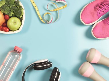 Üst ya da pembe spor ayakkabılar, pembe dambıllar, ölçüm bandı, kulaklık ve sebzeler mavi arkaplanda ve ortasında fotokopi alanı var. Çerçeve. sağlıklı yaşam tarzı geçmişi.