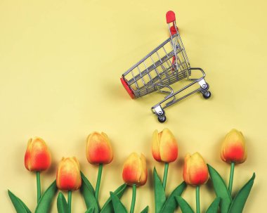 Sarı arka planda sarı kırmızı laleli alışveriş arabasının üstü ya da düzlüğü. Bahar alışveriş konsepti.