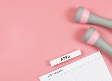 Üst ya da düz alışkanlık takip kitabı, ahşap takvim Nisan, gri pembe halterler, fotokopi alanı olan pembe arka plan. Kişisel gelişim ve aktif yaşam tarzı kavramı.