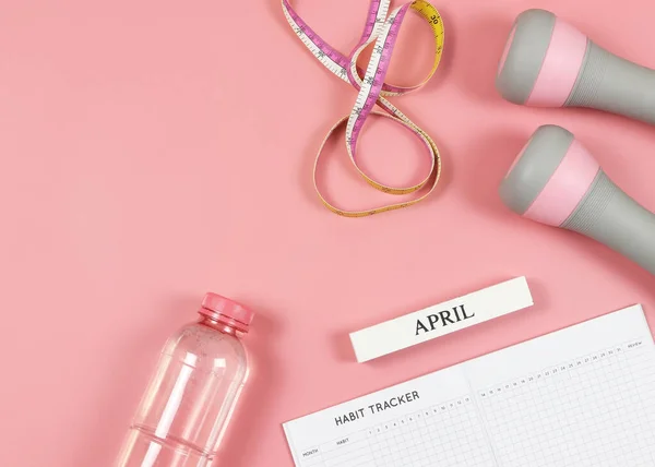 stock image Top view or flat lay of habit tracker book, wooden calendar April, gray pink dumbbells, bottle of water  and measuring tape on pink background with copy space. Self development and active lifestyle concept.