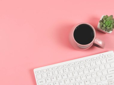 Üst ya da düz bilgisayar klavyesi, pembe kahve fincanı ve pembe arkaplanlı sulu bitki saksısı ve metin için fotokopi alanı. Kadınsı işyeri. Sabah rutini.