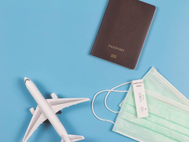 Mavi arka planda, uçak modeli ve pasaportlu tıbbi yüz maskeleri üzerindeki antijen test kiti (ATK) Covid-19 negatif çıktı. Yeni normal seyahat .