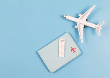 Mavi arka planda, uçak modeli ve kopyalama alanı ile pasaport kapağı üzerinde yapılan antijen test kiti (ATK) Covid-19 negatif test sonuçları. Yeni normal seyahat.