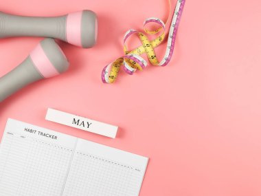 Üst görünüm ya da düz alışkanlık takip kitabı, tahta takvim Mayıs, gri pembe dambıllar ve pembe arka planda fotokopi alanı ile ölçüm bandı. Kişisel gelişim ve aktif yaşam tarzı kavramı.