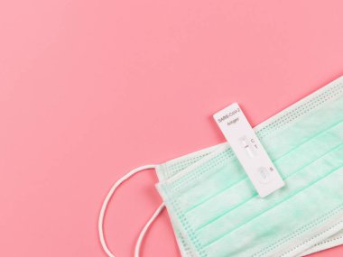 Covid-19 negatif test sonuçlarının (ATK) pembe arkaplandaki tıbbi yüz maskeleri üzerindeki antijen test kitinin üst görünümü veya düz yatışı.